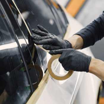 Auto body repair series. Masking car before repaint. Man in a black uniform.