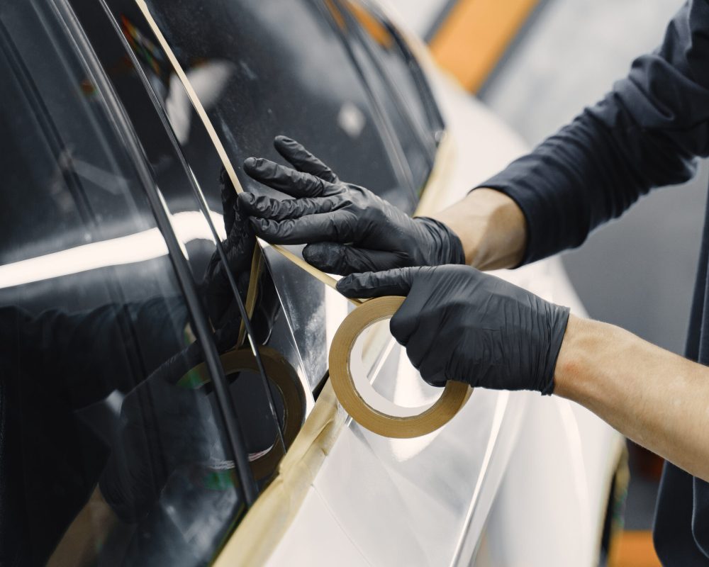 Auto body repair series. Masking car before repaint. Man in a black uniform.