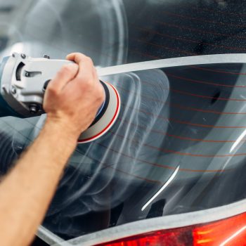 Worker with polishing machine removes the track from wiper blade on car window. Auto detailing on carwash service