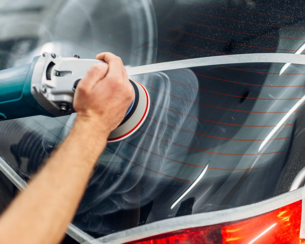 Worker with polishing machine removes the track from wiper blade on car window. Auto detailing on carwash service